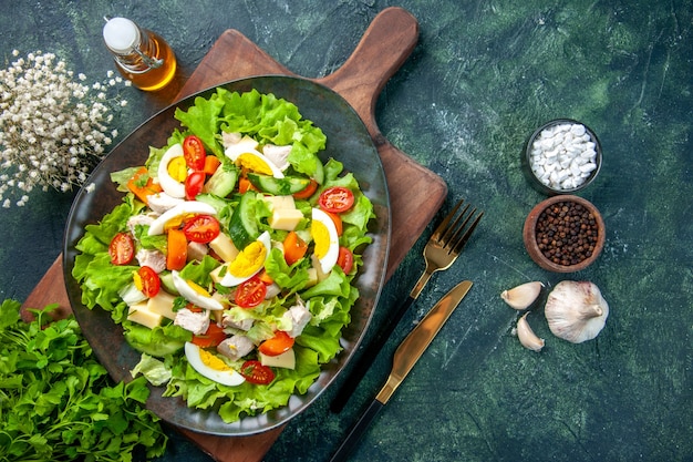 Vue horizontale de la délicieuse salade avec de nombreux ingrédients frais sur une planche à découper en bois épices bouteille d'huile ail couverts sur fond de couleurs mélange vert noir