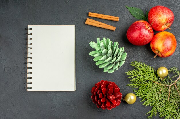 Vue horizontale du cahier et des pommes fraîches, des citrons verts à la cannelle et des accessoires de décoration sur fond noir