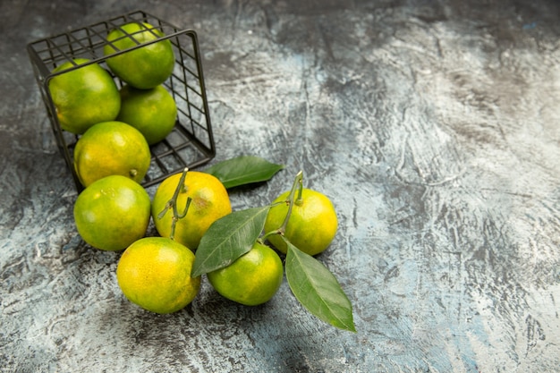 Photo gratuite vue horizontale du panier tombé avec des mandarines vertes fraîches coupées en deux et des mandarines pelées sur fond gris