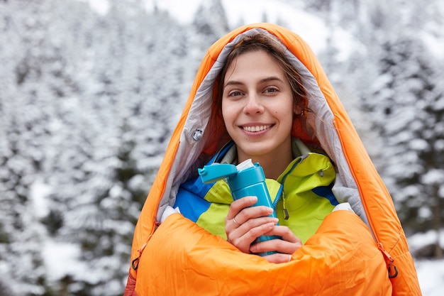 Vue horizontale du touriste attrayant souriant se sent froid après une expédition dans les montagnes enneigées