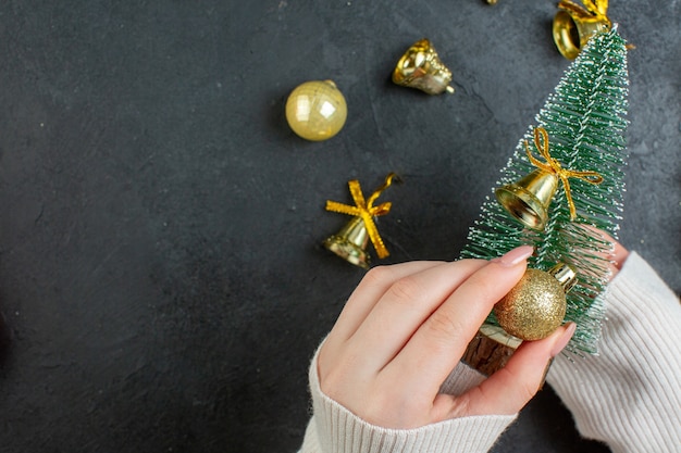 Vue horizontale de la main tenant l'arbre de Noël et accessoires de décoration sur table sombre