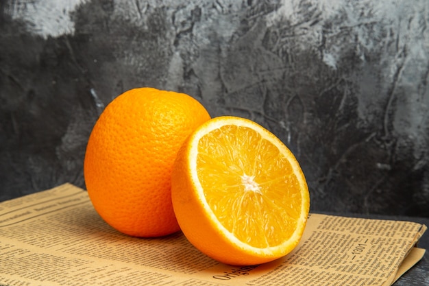 Photo gratuite vue horizontale d'oranges fraîches sous forme coupée et entière sur papier journal sur fond gris