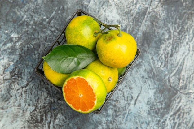 Vue horizontale d'un panier plein de mandarines vertes fraîches et coupées en deux mandarines sur fond gris