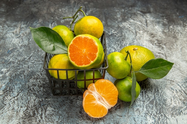 Vue horizontale d'un panier plein de mandarines vertes fraîches et coupées en deux et de mandarines pelées sur fond gris