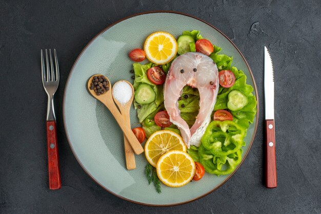 Vue horizontale de poisson cru et de légumes frais hachés tranches de citron épices sur une assiette grise et couverts sur une surface noire en détresse