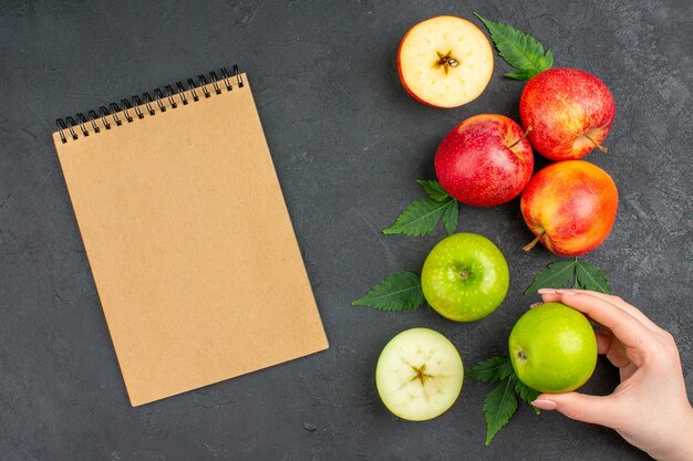 Vue horizontale de pommes et de feuilles naturelles fraîches entières et coupées et d'un cahier sur fond noir