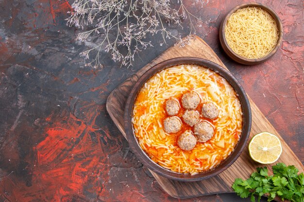 Vue horizontale d'une savoureuse soupe de boulettes de viande avec des nouilles à bord de feuilles de citron pâtes en bois un tas de légumes verts sur fond sombre