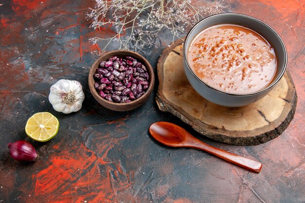 Vue horizontale de la soupe aux tomates classique dans un bol bleu sur le plateau en bois bouteille d'huile haricots ail oignon et citron sur table de couleurs mixtes