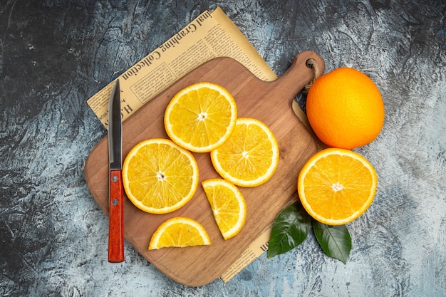 Vue horizontale de tranches de citron frais avec couteau sur planche à découper en bois sur papier journal sur fond gris