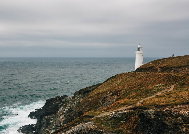 Photo gratuit vue imprenable sur un phare sur une colline couverte d'herbe au bord de l'océan par temps nuageux