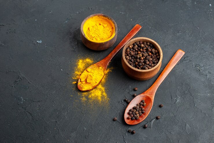 Photo gratuit vue inférieure poivre noir de curcuma dans de petits bols dans des cuillères en bois sur surface noire