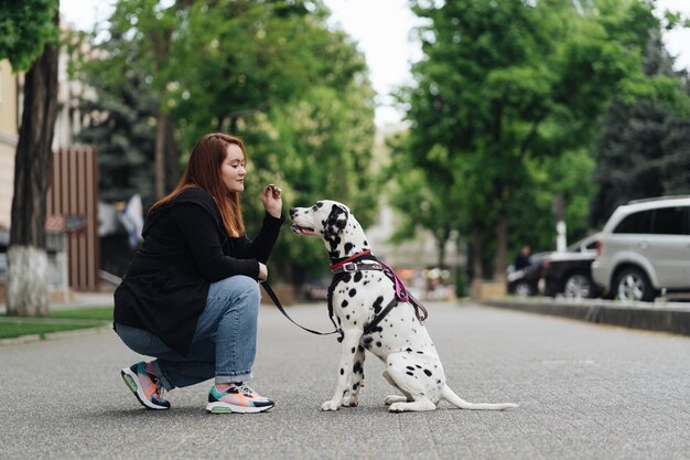 Vue sur une jeune femme de race blanche jouant et entraînant son chien dalmatien