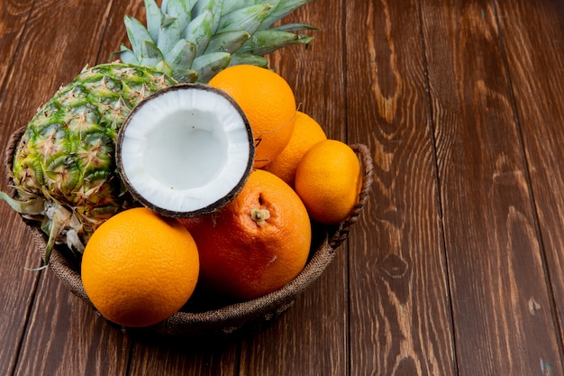 Vue latérale des agrumes comme ananas noix de coco orange mandarine dans le panier sur fond de bois avec copie espace