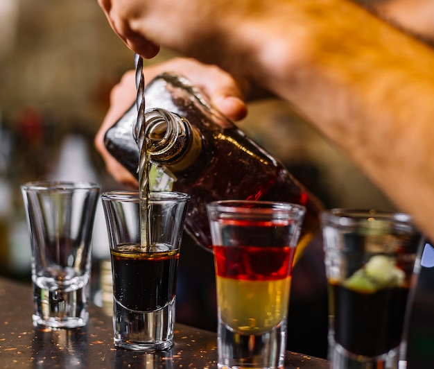 Photo gratuite vue latérale d'alcool multicolore coups d'alcool avec une tranche de kiwi sur la table