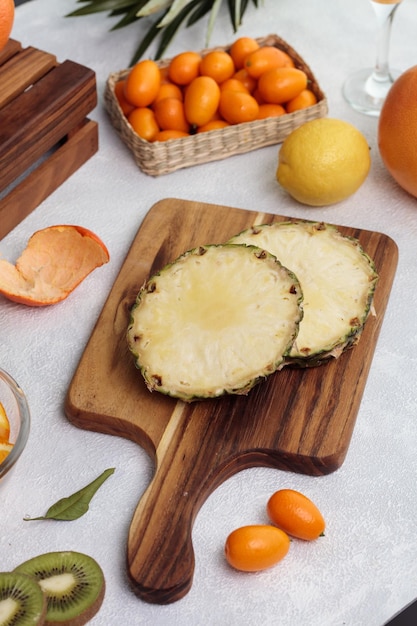 Vue latérale de l'ananas coupé sur une planche à découper avec kumquat citron orange avec couteau sur fond blanc