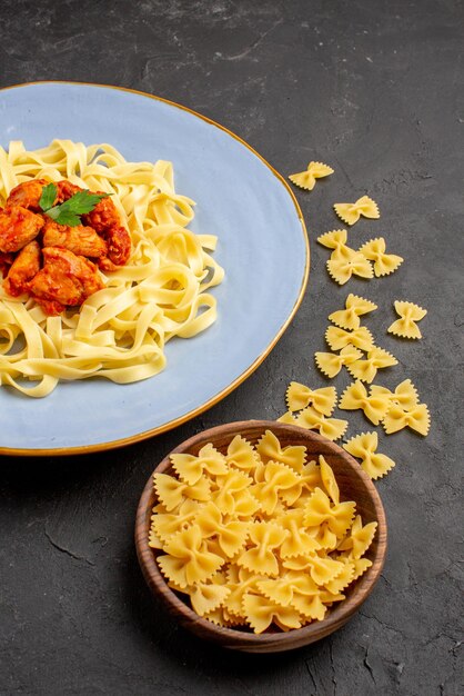 Vue latérale appétissante bol de pâtes à côté de l'assiette de pâtes appétissantes avec sauce et viande sur la table sombre