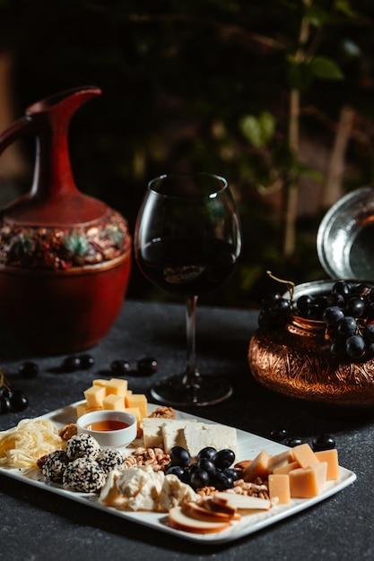 Vue latérale de l'assiette de fromage servi avec du raisin et du miel sur tableau noir