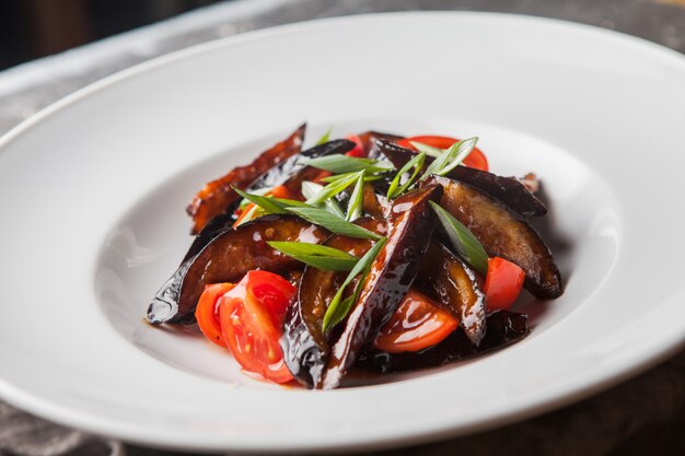 Vue latérale aubergine frite avec tomate et oignons verts hachés et chiffon en plaque blanche ronde