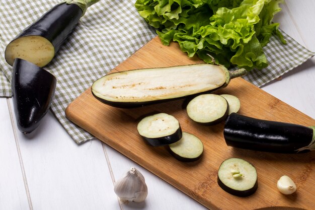 Vue latérale d'aubergines fraîches hachées à l'ail sur une planche avec des feuilles de salade