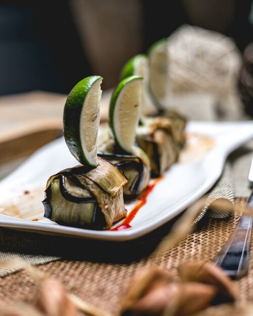 Vue latérale d'aubergines frites roulées avec des tranches de citron vert