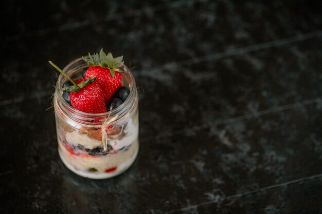 Vue latérale de l'avoine pendant la nuit avec des fraises fraîches, des bleuets et des noix dans un bocal en verre sur fond sombre avec copie espace