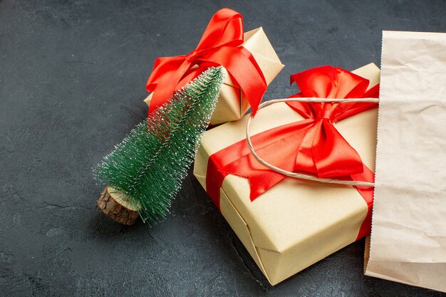 Vue latérale de beaux cadeaux avec ruban rouge et arbre de Noël sur une table sombre