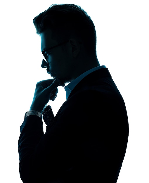 Vue latérale d'un bel homme réussi à lunettes portant en costume pensivement et regardant vers le bas tout en gardant la main avec une montre au poignet sur le menton et posant sur fond blanc