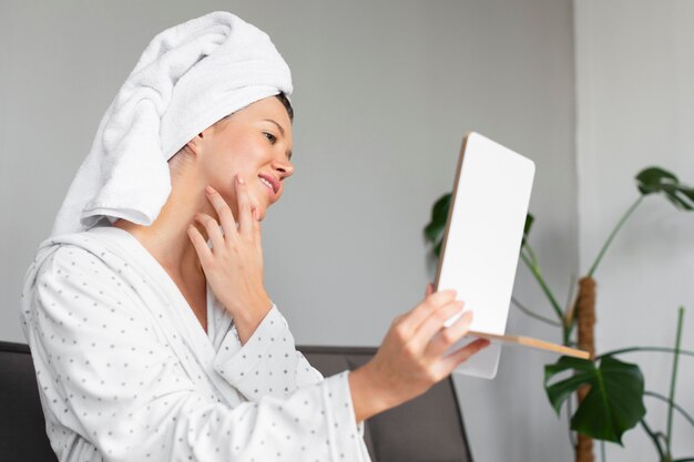 Vue latérale de la belle femme regardant dans le miroir tout en se livrant à des soins personnels