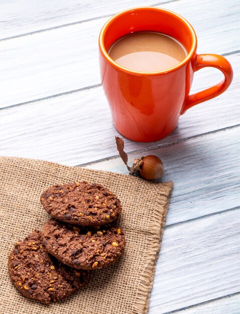 Vue latérale des biscuits à l'avoine avec des pépites de chocolat et des noix et une tasse de boisson au cacao sur un bois