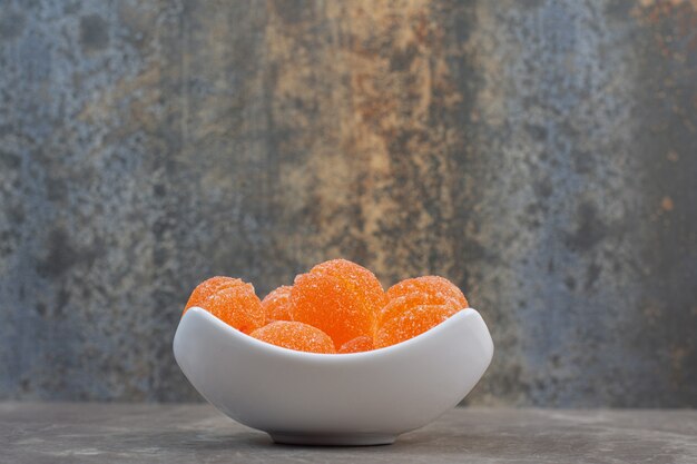 Vue latérale d'un bol en céramique blanche rempli de bonbons délicieux à l'orange.