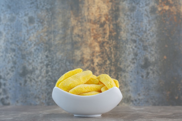 Vue latérale d'un bol en céramique blanche rempli de bonbons sucrés jaunes.