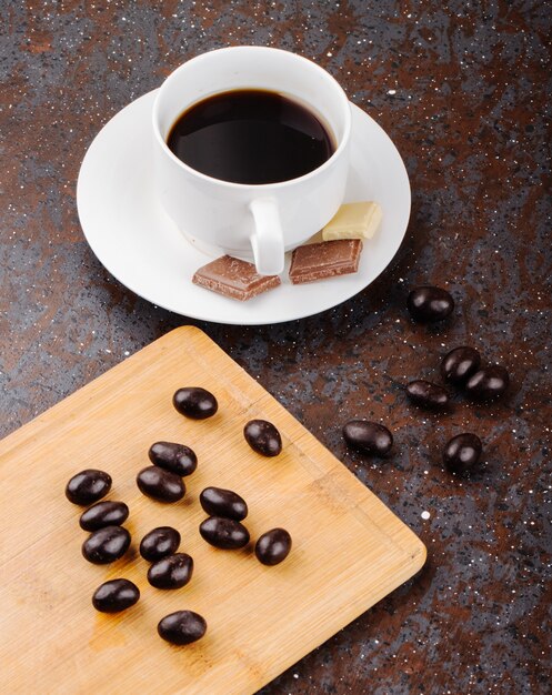 Vue latérale des bonbons aux noix au chocolat glacées éparpillés sur une planche de bois et une tasse de café sur fond noir