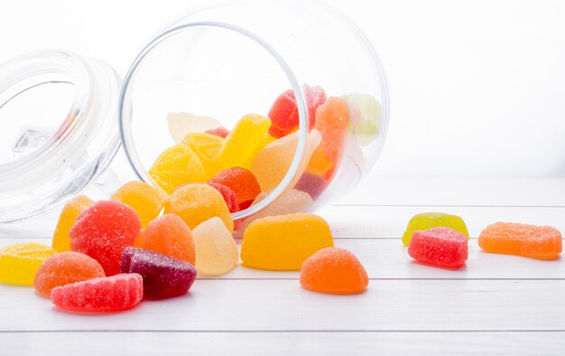 Vue latérale de bonbons colorés à la marmelade éparpillés dans un bocal en verre sur une surface en bois