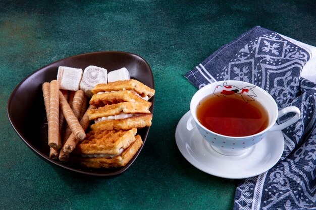 Vue latérale bonbons gaufres petits pains sucrés et marmelade avec une tasse de thé sur vert