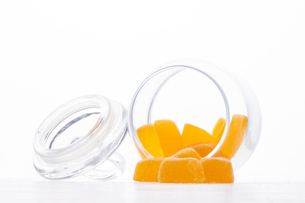 Vue latérale de bonbons à la marmelade jaune éparpillés dans un bocal en verre blanc