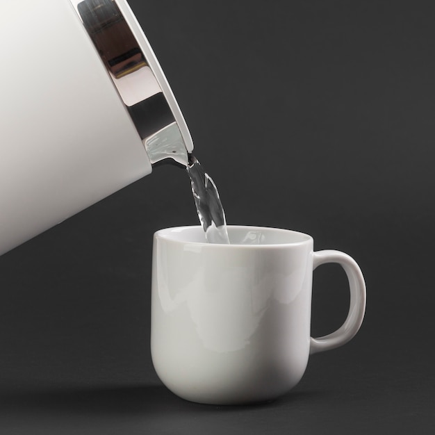 Photo gratuite vue latérale d'une bouilloire électrique verser de l'eau dans une tasse