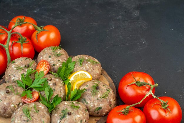 Vue latérale des boulettes de viande non cuites sur une planche à découper en bois tomates avec tiges sur fond de vague sombre avec espace libre