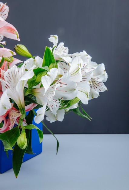 Vue latérale d'un bouquet de fleurs d'alstroemeria de couleur rose et blanc dans une boîte bleue sur fond gris