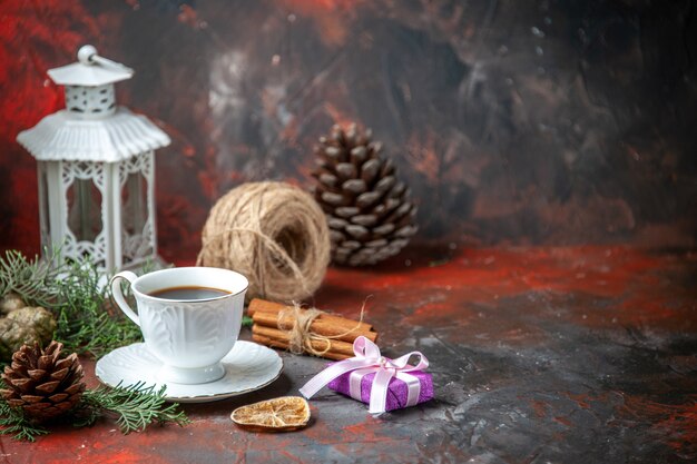 Vue latérale des branches de sapin citron vert cannelle cône de conifère une boule de corde une tasse de thé noir sur fond rouge