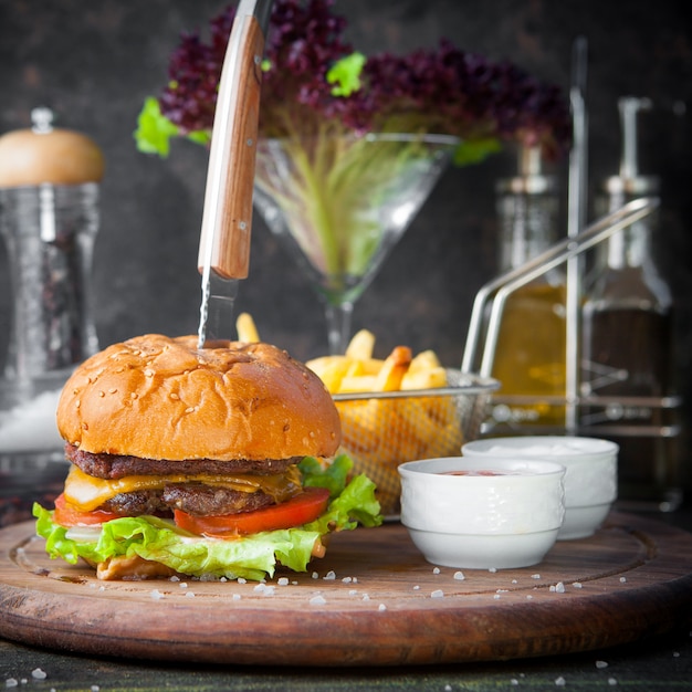 Vue latérale burger avec frites et bol pour sauce et couteau dans un plateau en bois sur le restaurant