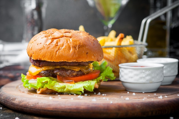 Vue latérale burger avec frites et bol pour sauce et panier de friture dans un plateau en bois sur le restaurant