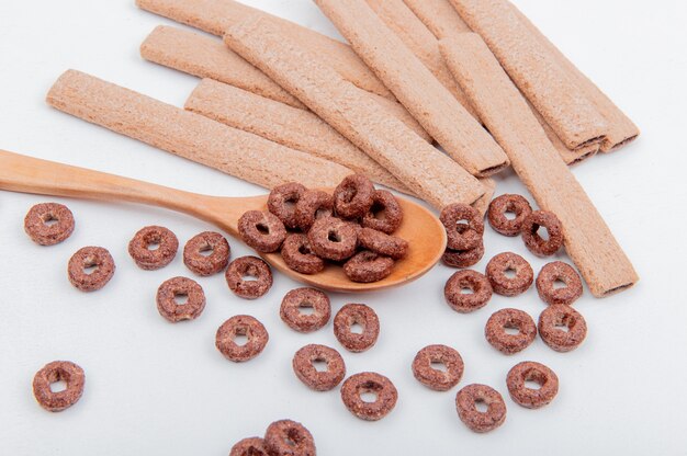 Vue latérale des céréales dans une cuillère en bois et des cookies sur une surface blanche