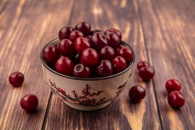 Vue latérale des cerises dans un bol et sur fond de bois