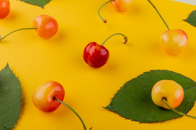 Photo gratuite vue latérale des cerises pluviales mûres fraîches avec des feuilles vertes sur jaune