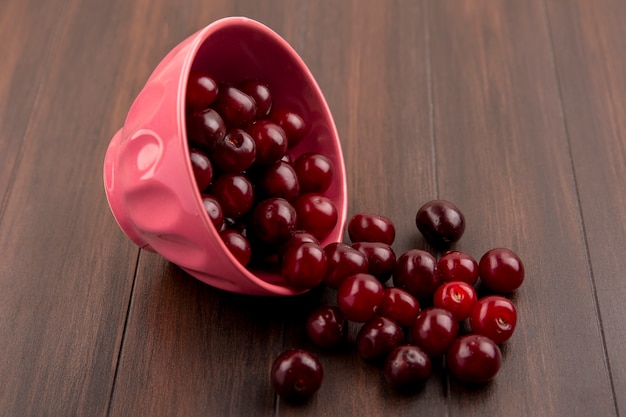 Vue latérale des cerises s'échappant du bol sur fond de bois