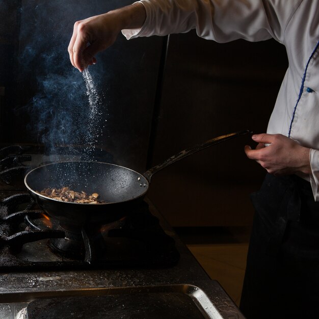 Vue latérale champignon frire avec sel et feu et main humaine dans la casserole