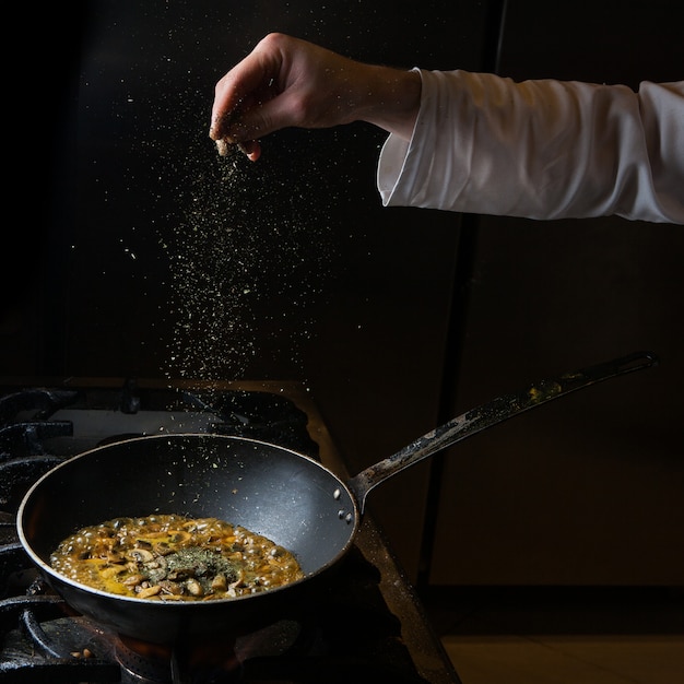 Vue latérale champignon friture avec poêle et menthe sèche et main humaine dans la casserole