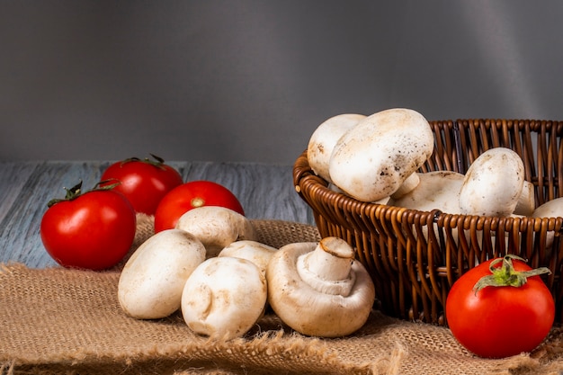 Vue latérale de champignons frais champignon dans un panier en osier et tomates fraîches sur un sac