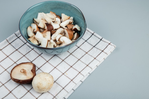 Vue latérale des champignons tranchés dans un bol sur une serviette à carreaux sur bleu clair