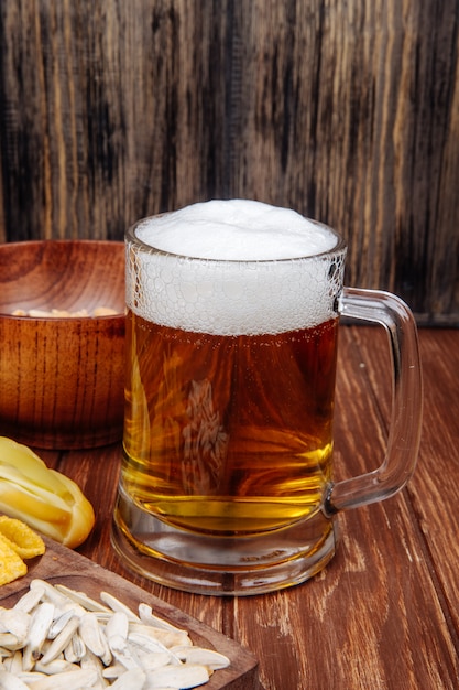 Vue latérale d'une chope de bière avec diverses collations salées sur rustique